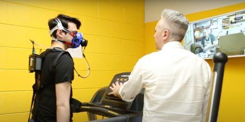 Student talks to research participant who is walking on treadmill while wearing mask apparatus